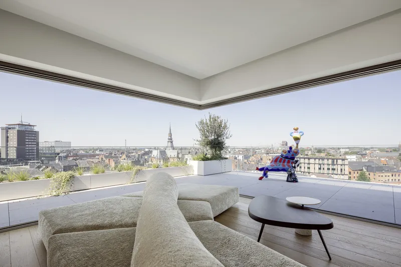 Corner glazed penthouse living room opening to a terrace with cityscape views and church spires on the horizon