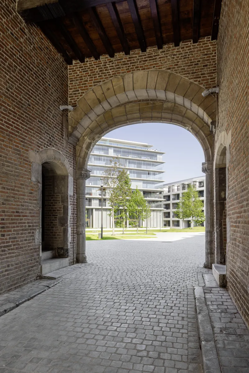 View through a stone archway with red brick walls framing the new terraced residential block and lawn beyond
