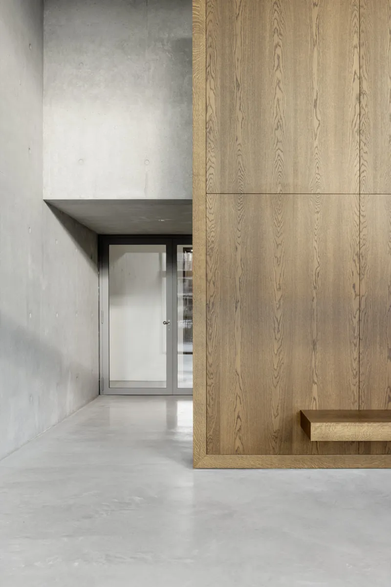 Entry vestibule with polished concrete floor meeting oak-clad wall and recessed threshold beneath angled soffit