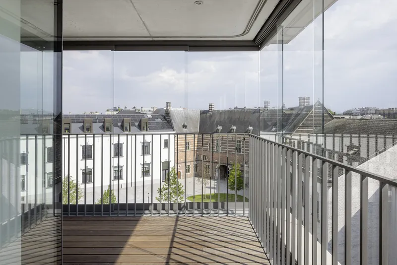 Glass-enclosed balcony with vertical metal railing and timber decking under overcast sky