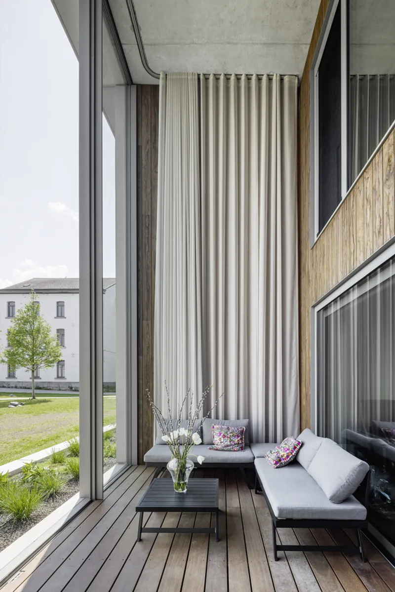 Timber-decked balcony with pleated fabric screen and seating overlooking courtyard with young trees
