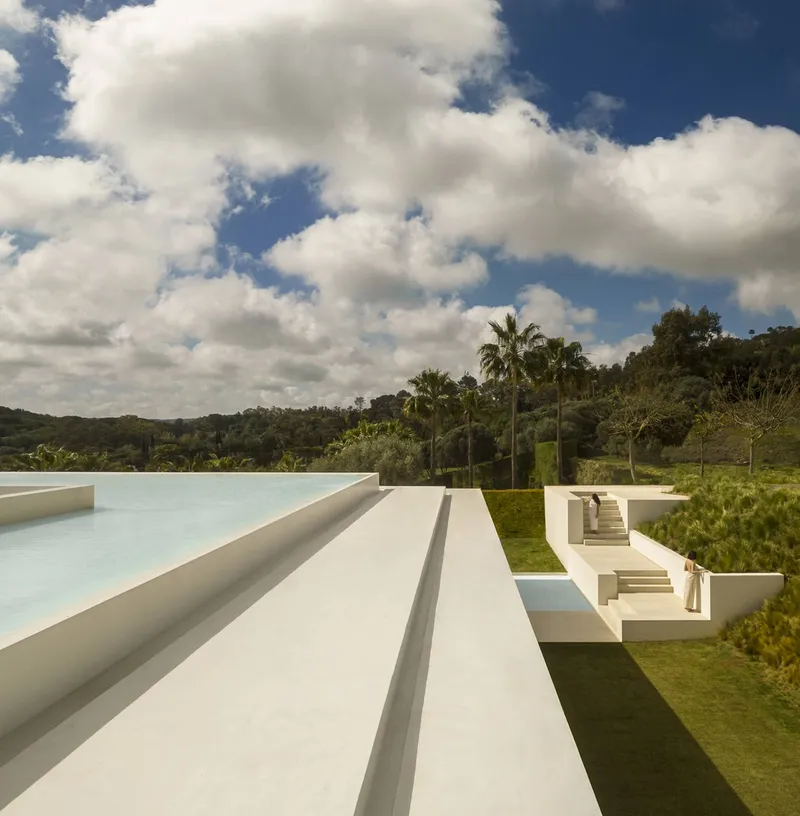 White terraced volumes stepping down the lawn toward palm trees under a cloudy sky