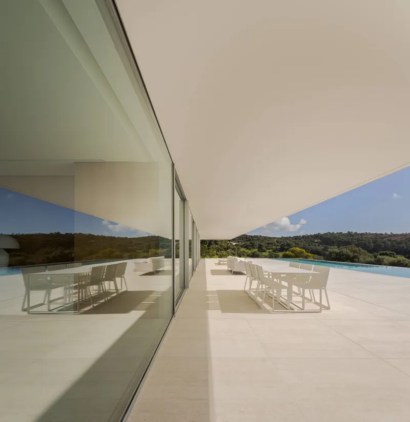 Outdoor terrace with white dining furniture beneath a deep overhang and reflected in the glazing