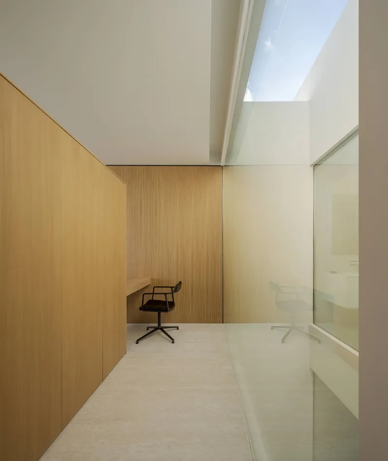 Light-filled study with vertical timber paneling and a single office chair beneath a rectangular skylight