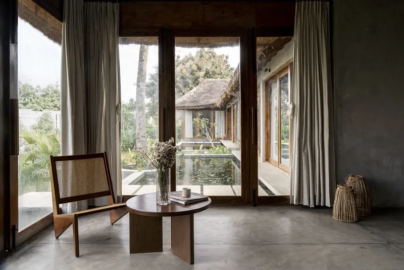 Polished concrete floor interior with cane chair and low table facing glass doors to courtyard pond