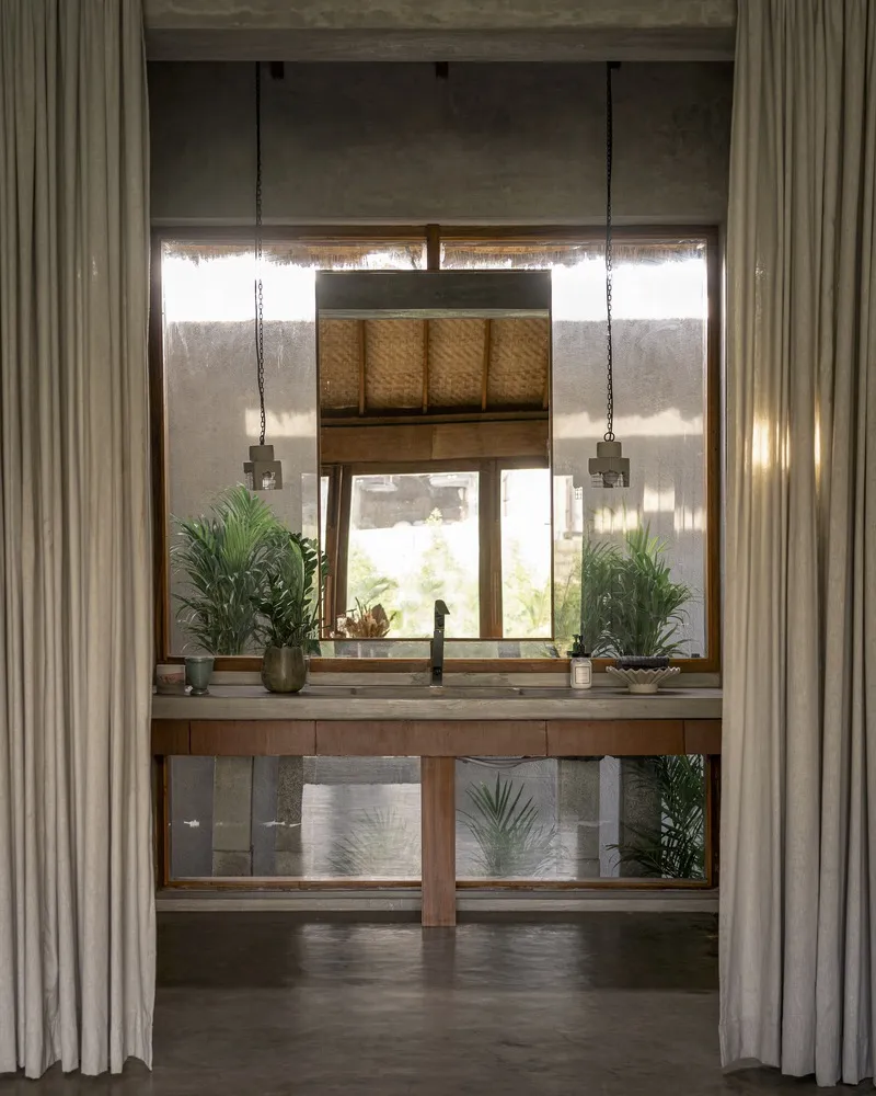 Bathroom vanity framed by curtains with pendant lights and window overlooking lush greenery beyond