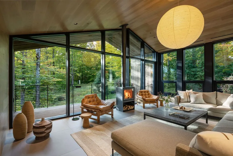 Living room with floor-to-ceiling glass walls, wood stove, and views to the forest deck