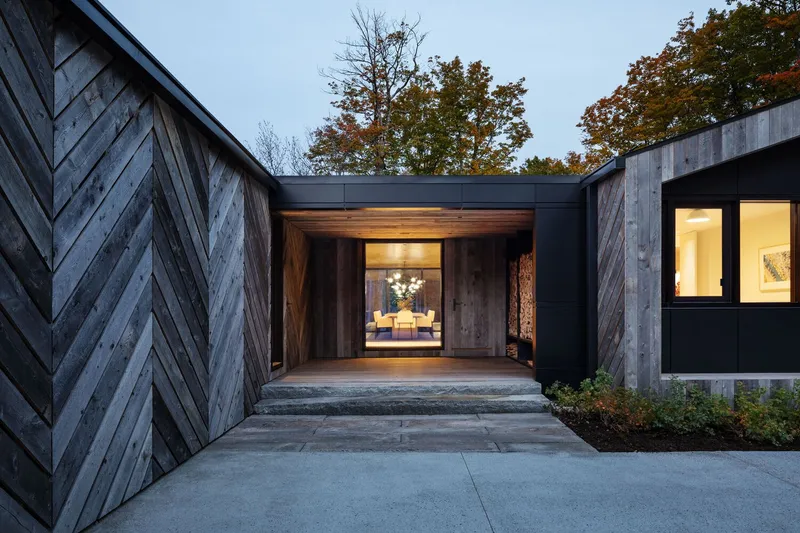 Entry courtyard with chevron timber cladding and timber-lined passageway leading to illuminated interior