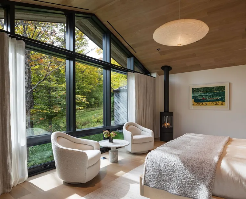 Bedroom with wood ceiling, black-framed clerestory windows and freestanding wood stove beneath pendant light