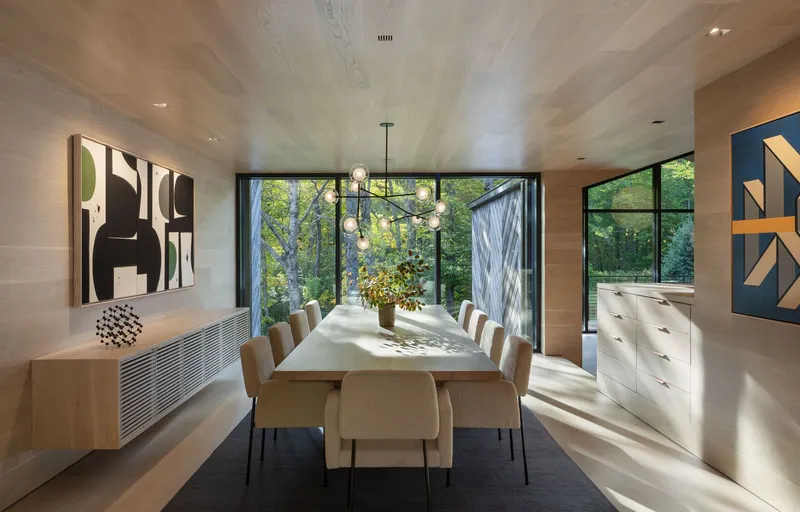 Dining room with pale wood ceiling and full-height glazing framing autumn foliage outside