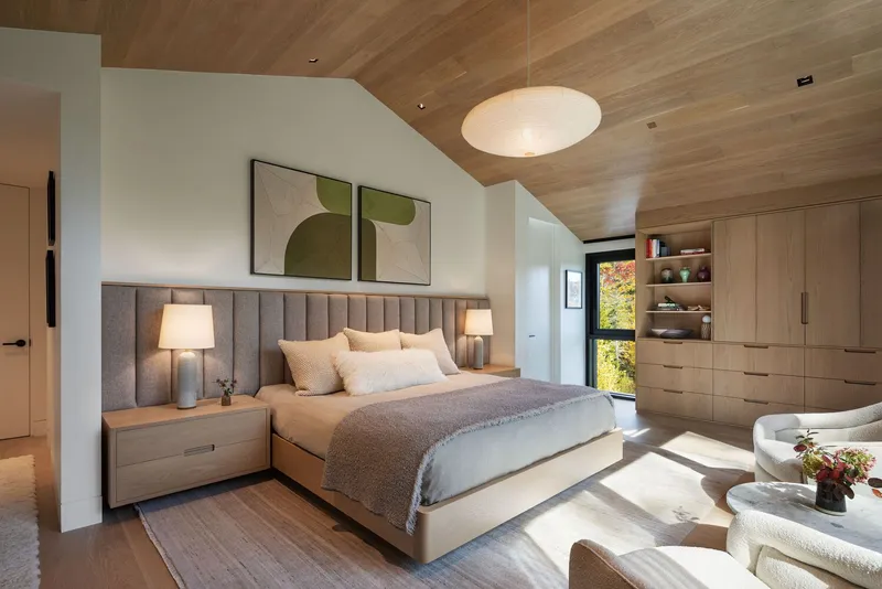 Bedroom with upholstered headboard, wood ceiling, and built-in cabinetry lit by afternoon sun