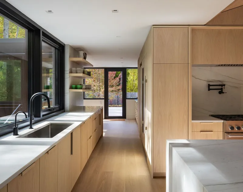 Galley kitchen with white stone counters, oak cabinetry, and glazed door framing autumn trees