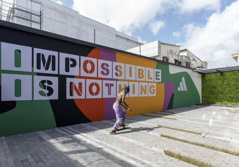 Painted exterior wall with graphic lettering and a figure walking across the paved plaza