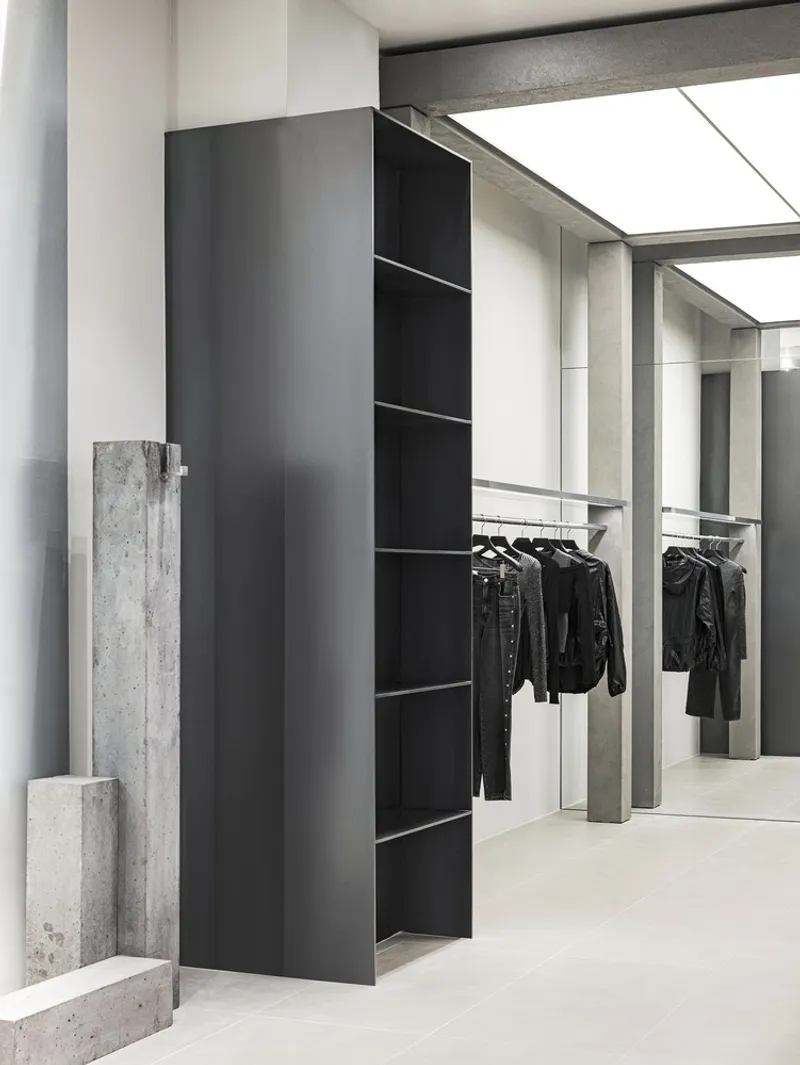 Black metal shelving unit flanked by raw concrete slabs against a pale tiled floor