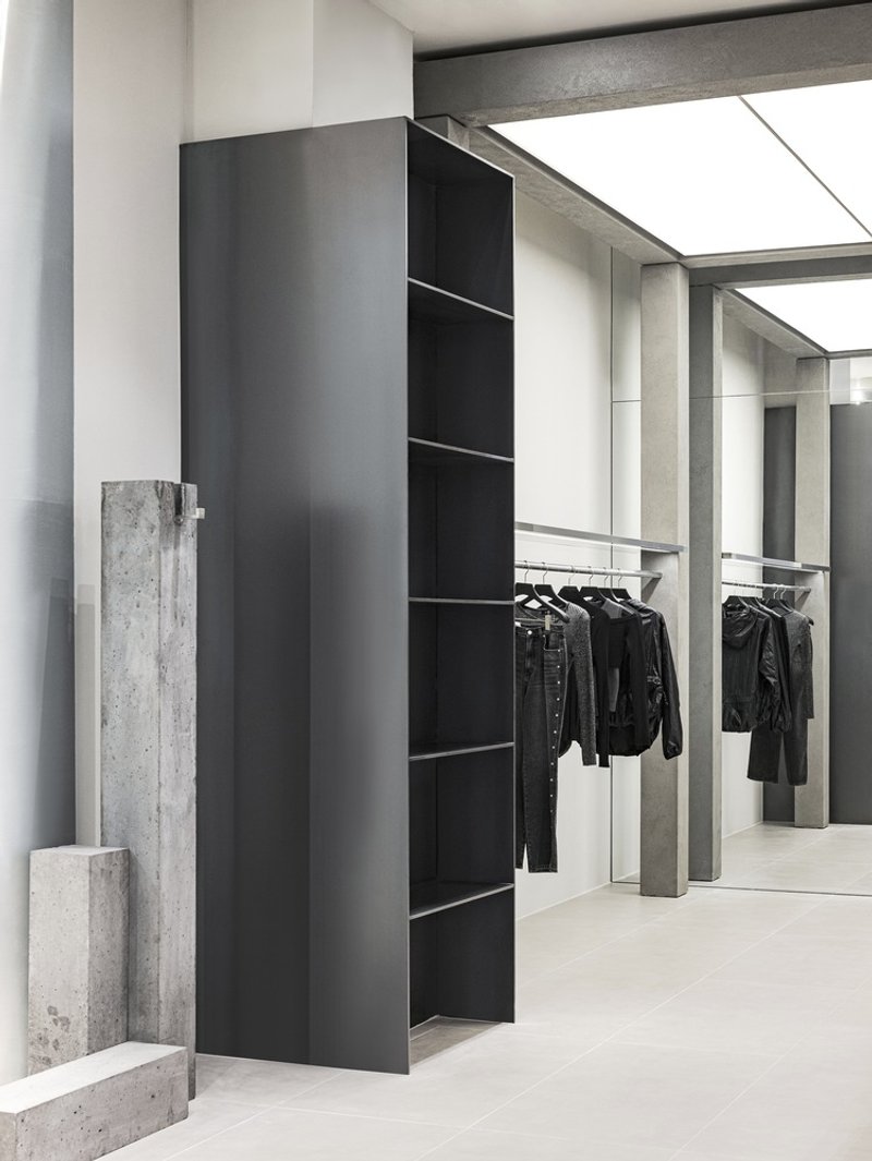 Black metal shelving unit flanked by raw concrete slabs against a pale tiled floor