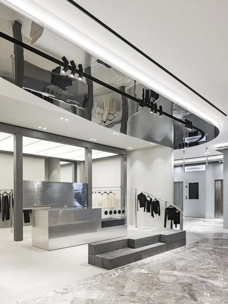 Double-height retail interior with mezzanine balcony, concrete display platforms and brushed steel fixtures