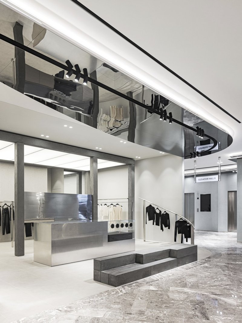 Double-height retail interior with mezzanine balcony, concrete display platforms and brushed steel fixtures