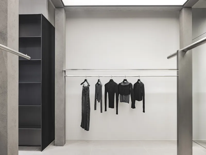 Fitting room alcove with steel hanging rail, concrete side walls and black display shelving