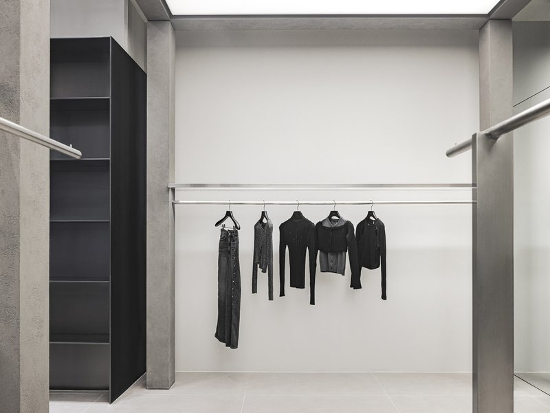 Fitting room alcove with steel hanging rail, concrete side walls and black display shelving