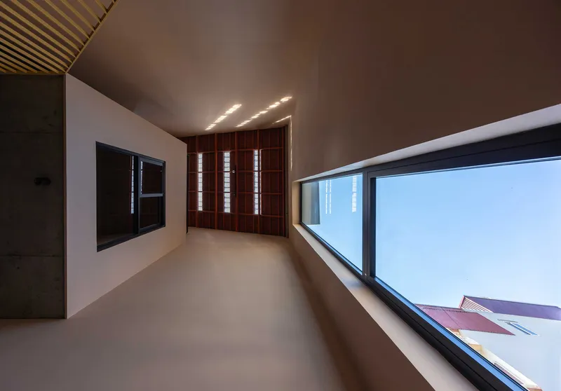 Corridor with angled glazing opening to sky and slatted timber wall with recessed lighting