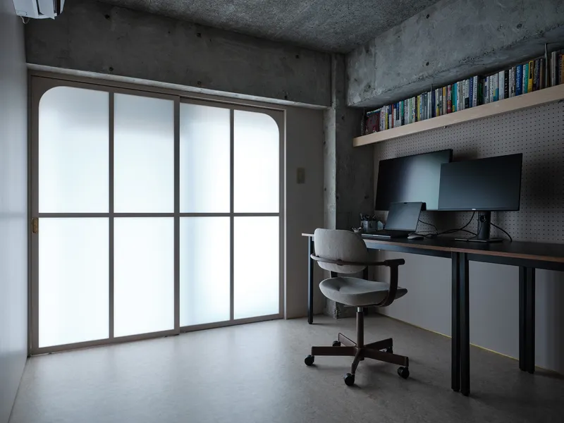 Workspace with arched translucent window, concrete walls and pegboard backing the desk