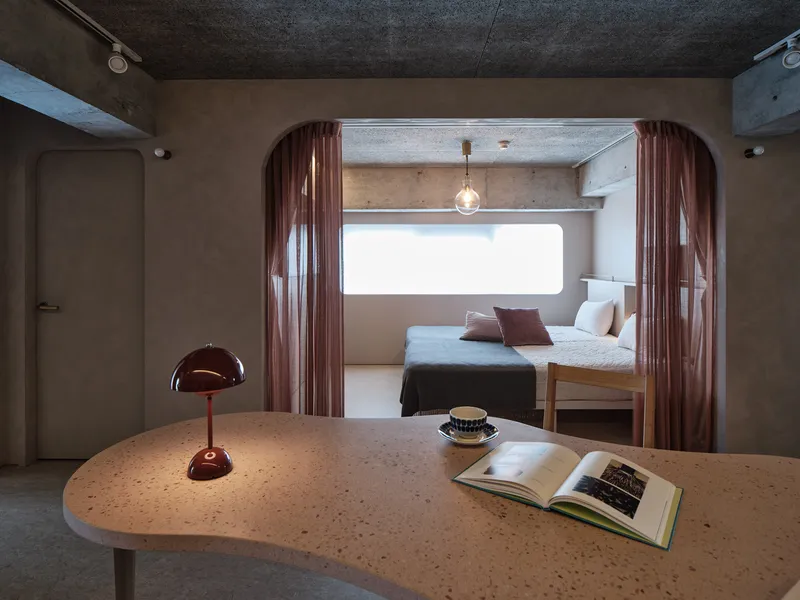 View through arched opening with rose curtains toward bedroom alcove with terrazzo table in foreground