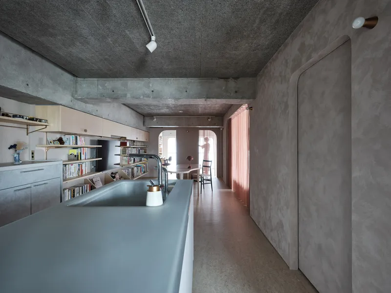 Long galley kitchen with concrete ceiling beam and rose curtains framing distant bedroom