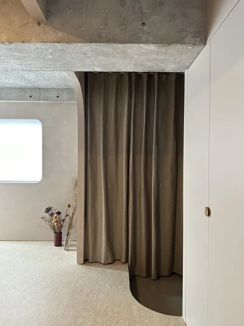 Curved brown fabric curtain suspended from exposed concrete ceiling near dried flowers in glass vases