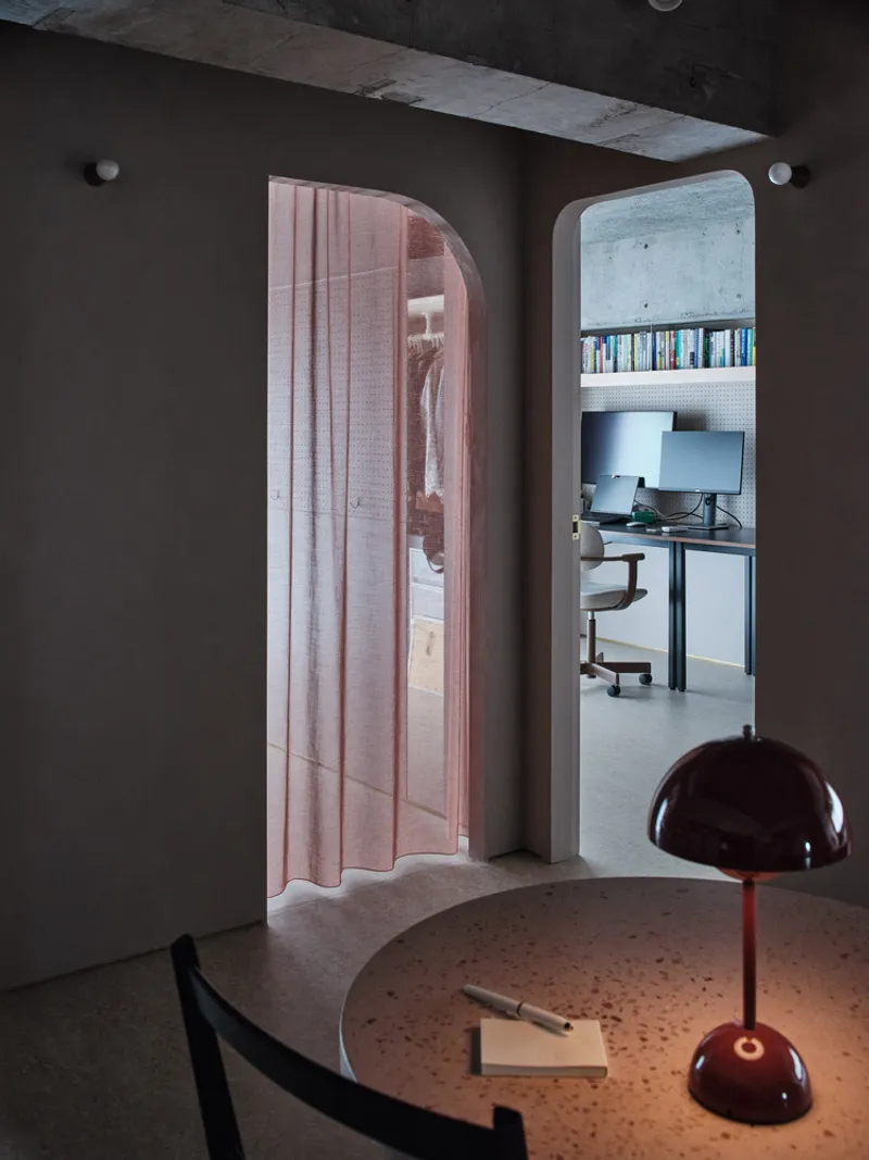Two arched openings framing bedroom with rose curtain and office with concrete walls