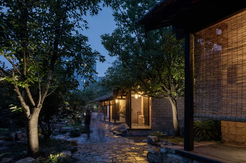 Glazed entrance pavilion with thatched roof and bamboo screen under trees at night