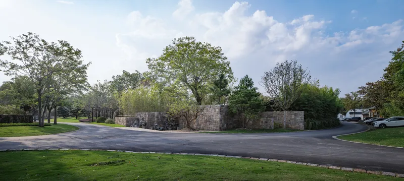 Low stone wall running along a curved asphalt road bordered by grass and mature trees