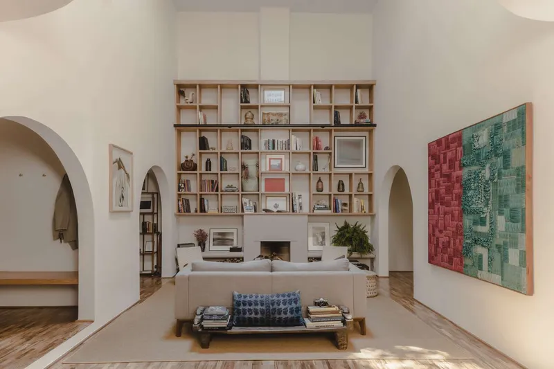 Living room with floor-to-ceiling timber bookshelf flanking central fireplace and arched doorways at either side