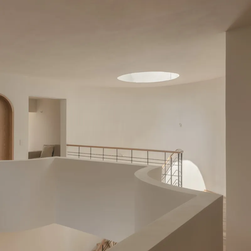 Upper floor landing with metal railing and circular skylight opening to double-height space below