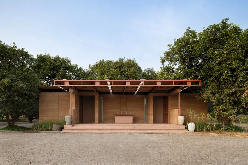 Timber-clad pavilion with exposed rafter pergola and central bench, framed by mature trees
