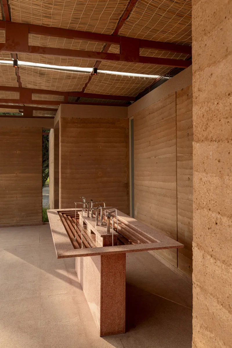Interior view of the communal sink counter with rammed earth walls and woven ceiling panels