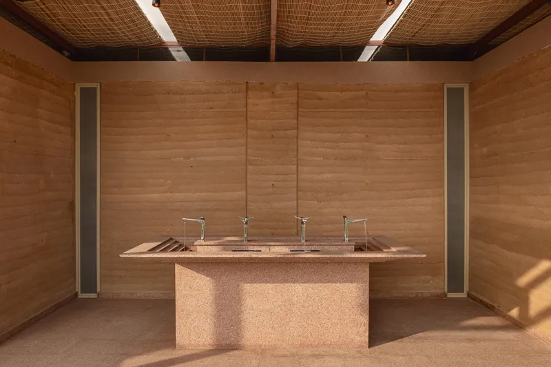 Interior showing the rammed earth walls, woven ceiling and central sink with afternoon sunlight