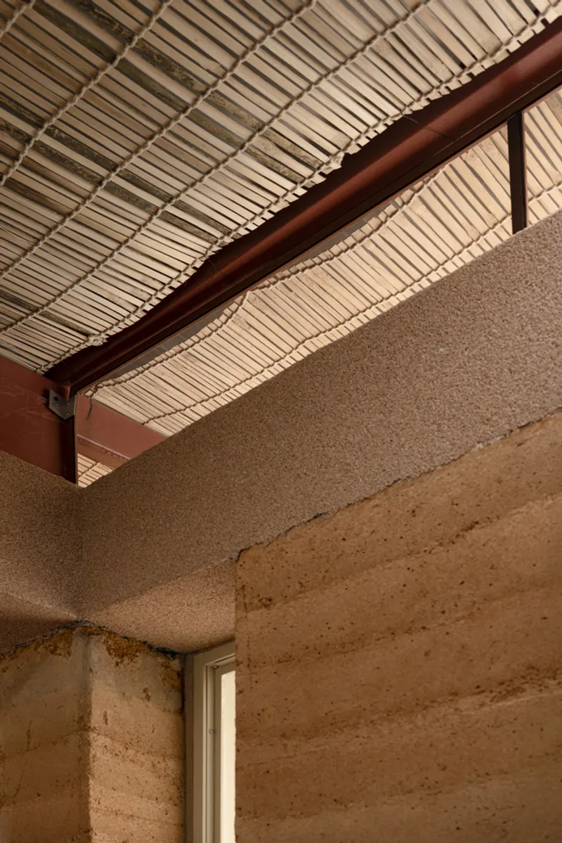 Junction of steel beam, rammed earth wall and bamboo ceiling under the timber pergola