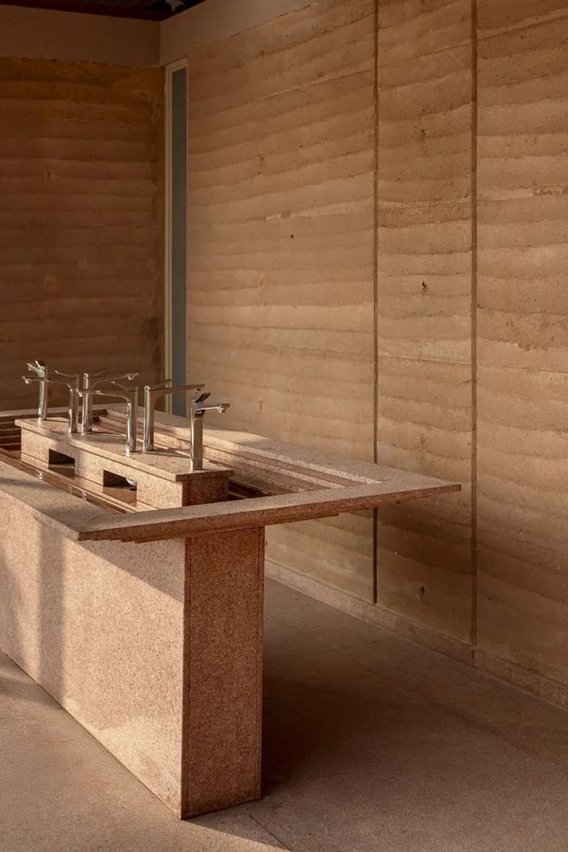 Interior view of the cantilevered sink counter with chrome fixtures against horizontal rammed earth walls