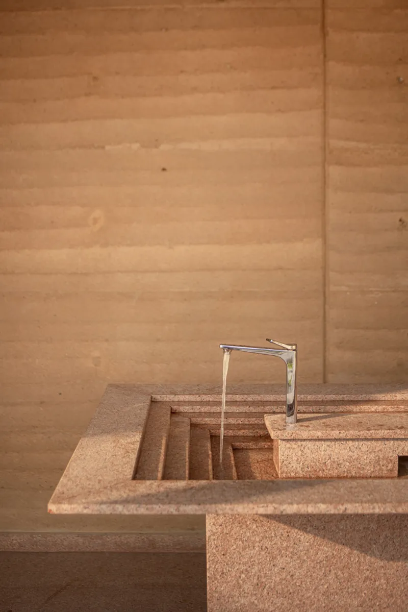Close-up of the chrome faucet and layered aggregate counter edge against rammed earth wall