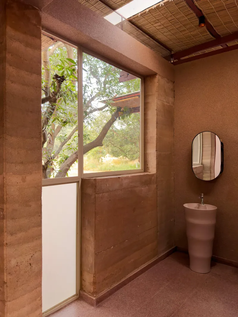 Interior bathroom with rammed earth walls, woven bamboo ceiling and tall window framing a tree outside