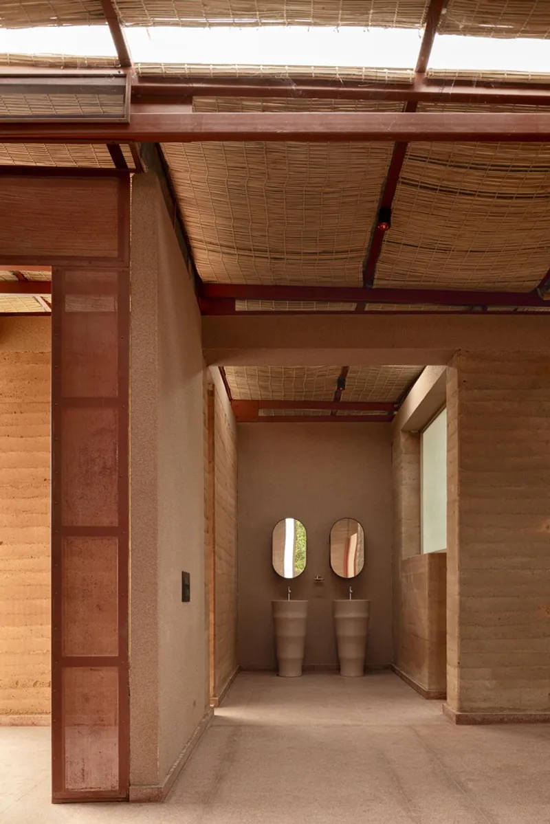 Corridor view into the restroom with oval mirrors, freestanding sinks, and woven bamboo ceiling above
