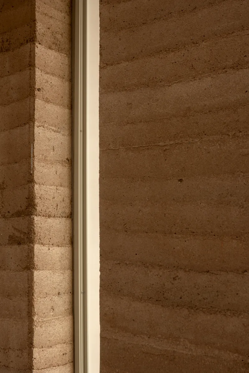 Detail of a metal window frame embedded in the layered rammed earth wall