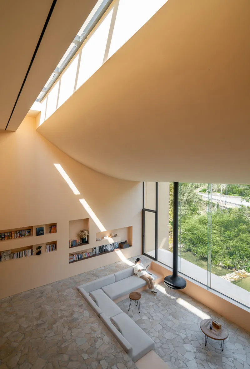 Double-height living room with clerestory windows casting afternoon light across built-in bookshelves and a sectional sofa