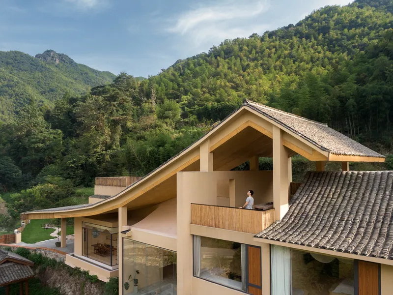 Gabled timber-framed terrace with a person standing at the balcony rail overlooking forested mountains