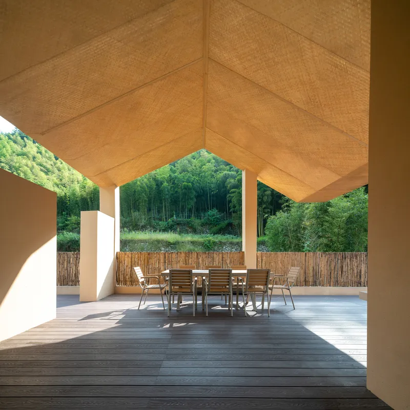 Covered timber deck terrace with dining table under a woven bamboo ceiling opening to forest