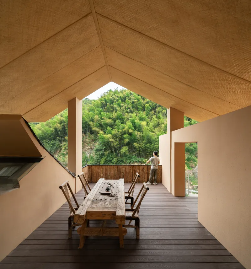 Gabled outdoor terrace framing a view of the wooded hillside with a person at the bamboo fence