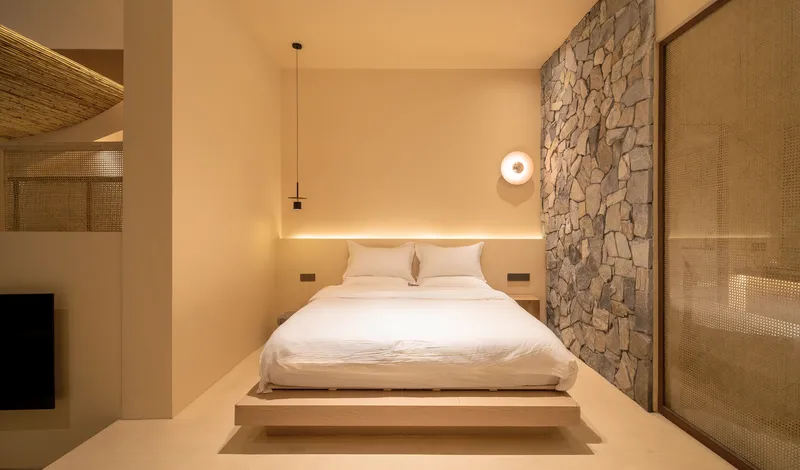 Bedroom with platform bed framed by irregular stone wall and recessed ceiling lighting