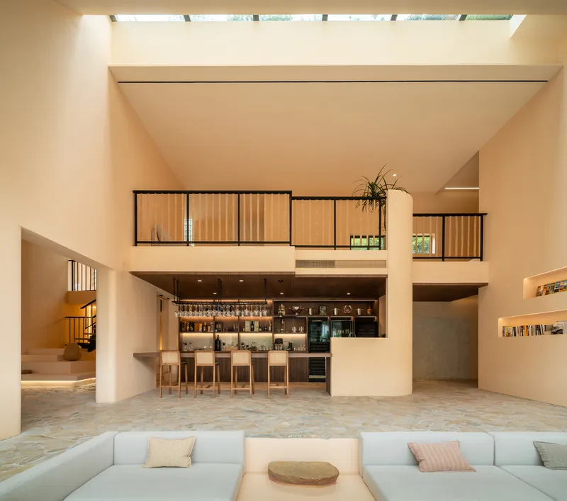 Double-height lobby with bar counter beneath suspended timber screens and skylights above