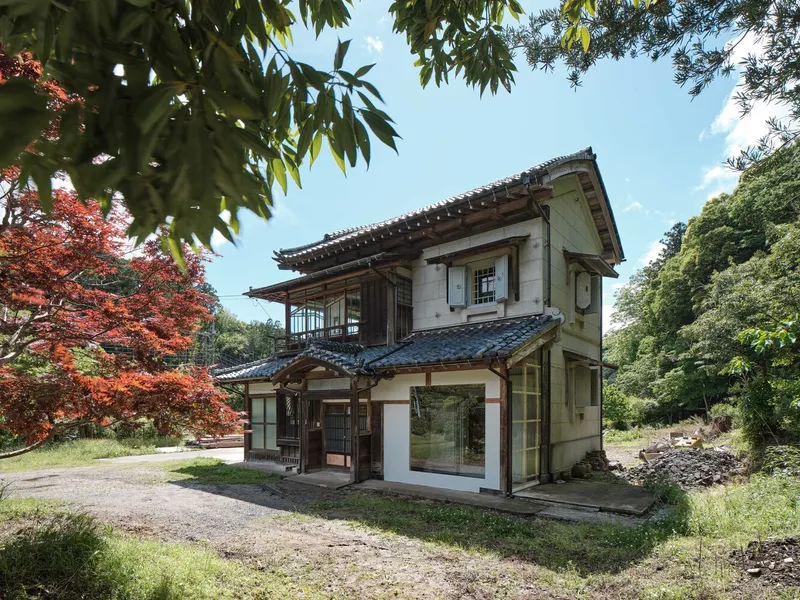 Two-story timber structure with tiled roof and white stucco walls framed by red maple foliage