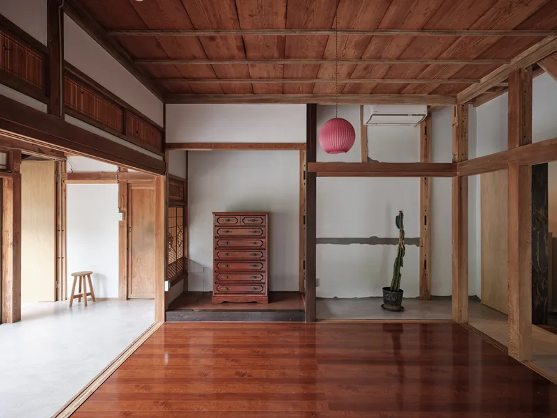 Interior corner with exposed timber frame, red chest of drawers, and polished wood floor meeting concrete